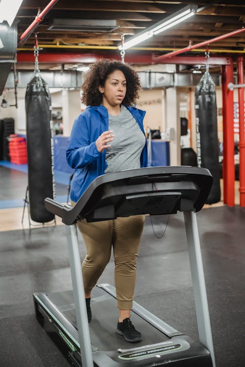 Free Full body of curvy black female running on treadmill during fitness workout in gym Stock Photo
