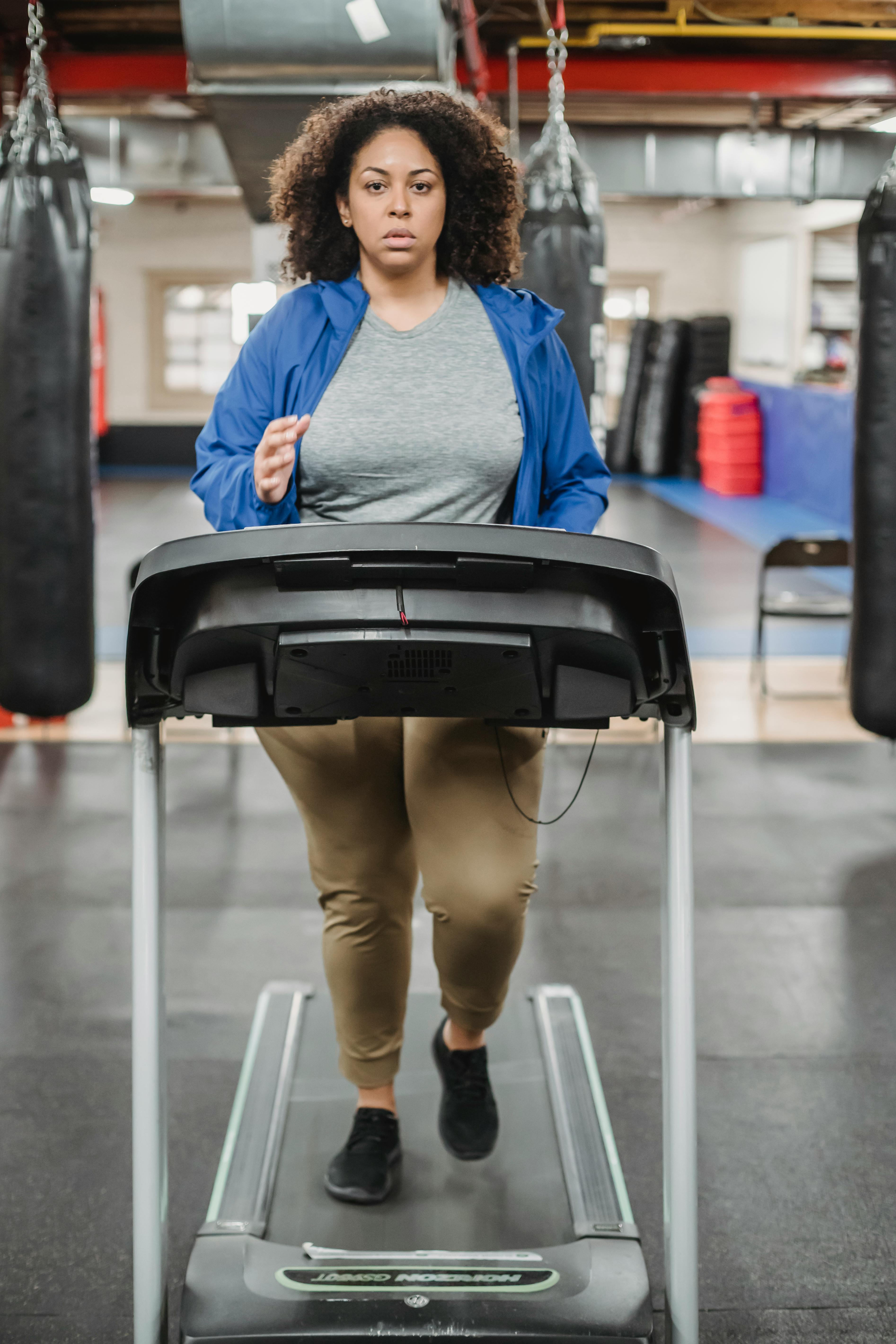 thoughtful woman training on treadmill in fitness club