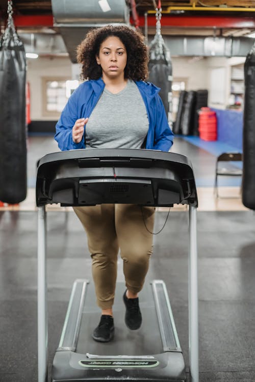 Free Full body of overweight female running on treadmill during workout and looking at camera Stock Photo