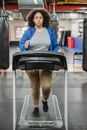 Full body of overweight female running on treadmill during workout and looking at camera