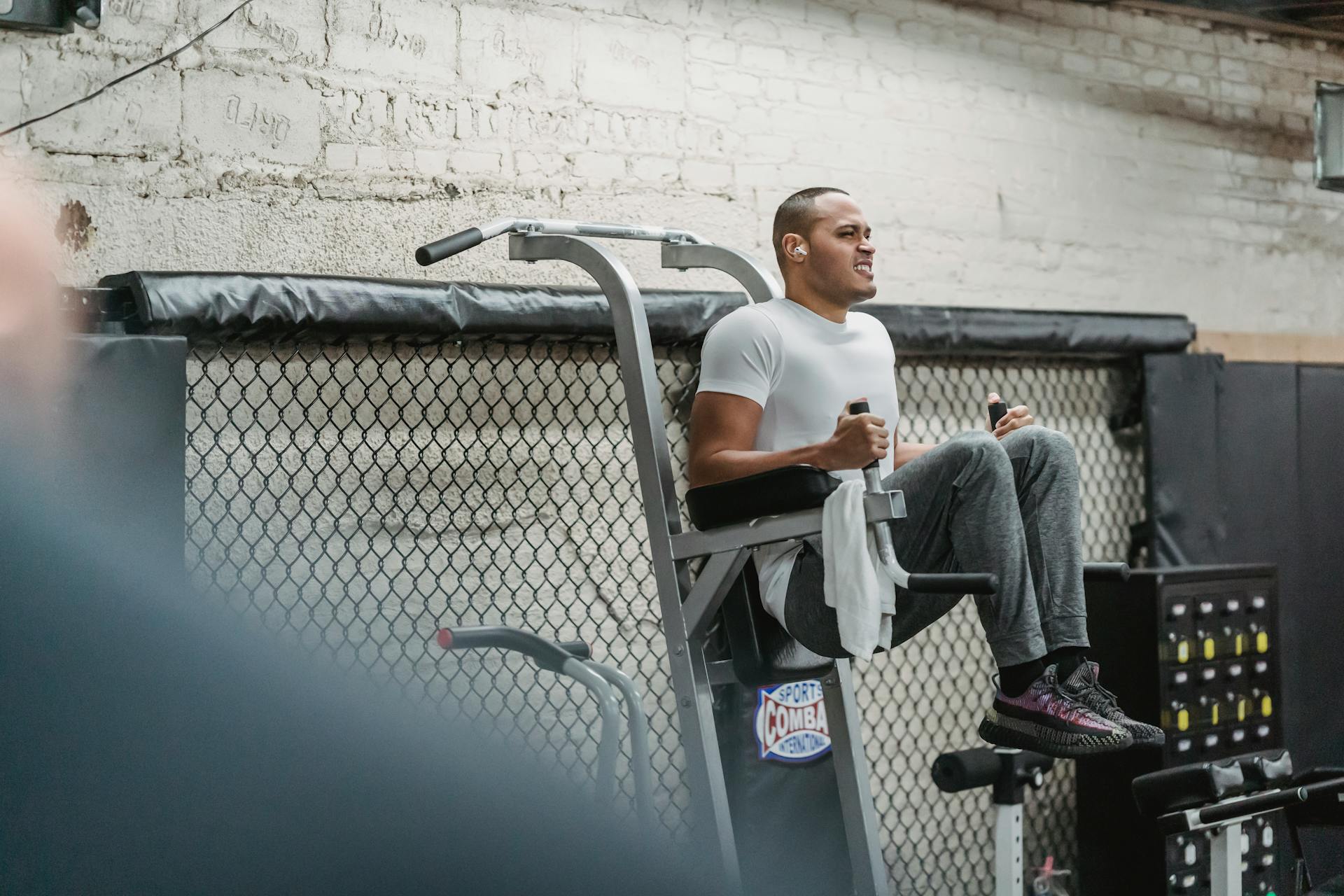 Full body of concentrated black athlete doing abdomen exercise knee to chest on sports machine in modern fitness club