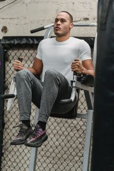 Full body of determined male athlete using exercise machine for knee to chest exercise during intense training in contemporary gym