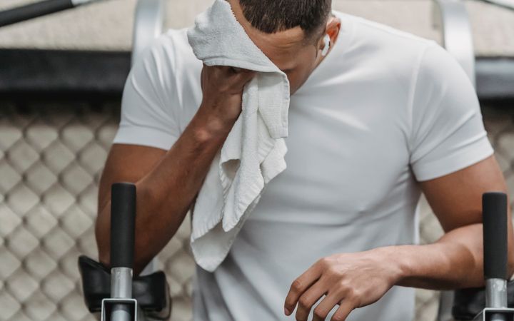 Weary black sportsman resting while wiping face with towel in modern sport club