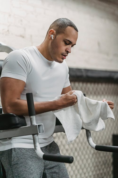 Free Strong sportsman with towel in hands resting after exercising on machine in modern gym Stock Photo