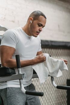 Strong sportsman with towel in hands resting after exercising on machine in modern gym