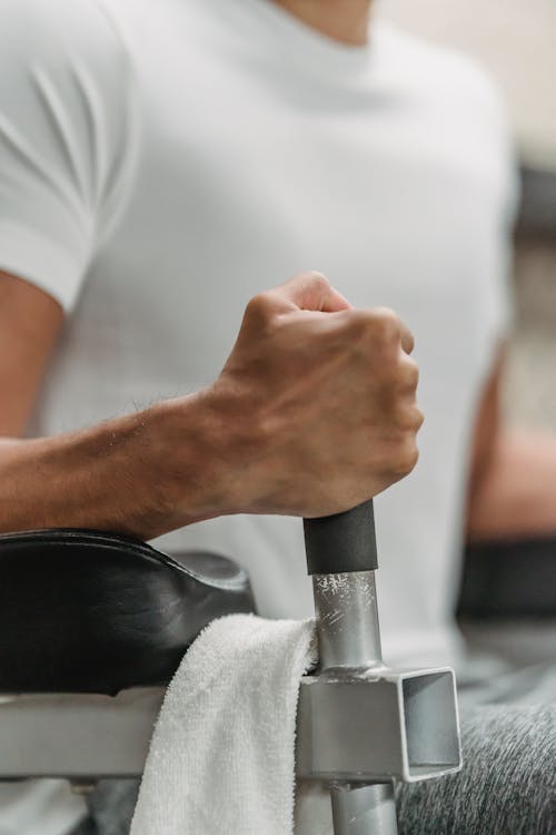 Crop unrecognizable muscular ethnic sportsman in white t shirt training in gym in daylight