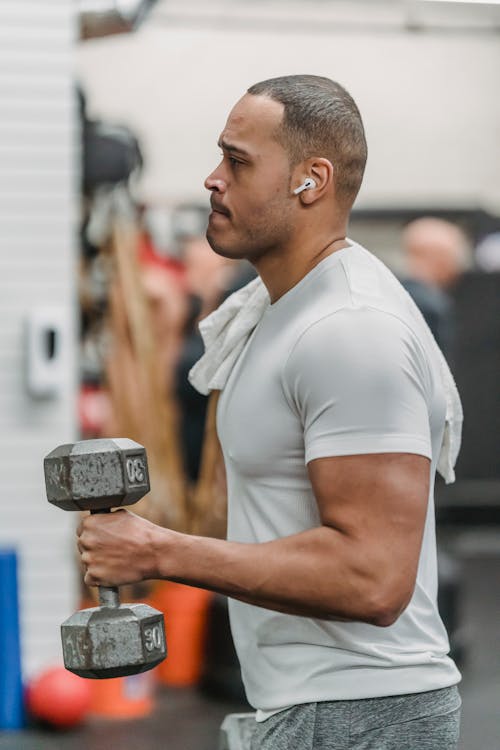 Side view of strong muscular African American sportsman in sportswear training with dumbbells in gym