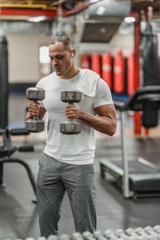 Young muscular male in sportswear doing exercise with dumbbells during intense training in contemporary fitness club