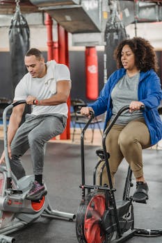 Two adults exercising together on stationary bikes in a modern gym setting.