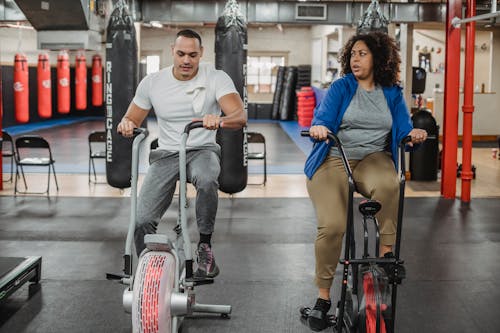 Free Full body of overweight black woman sitting on cycling machine and looking at fitness trainer Stock Photo