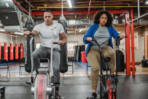 Full body of focused curvy female and muscular male instructor training on exercise bikes in spacious gym