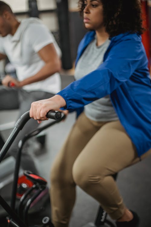 Crop plump black woman riding stationary bike in gym