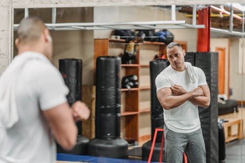 Wistful ethnic sportsman looking at biceps reflecting in gym mirror