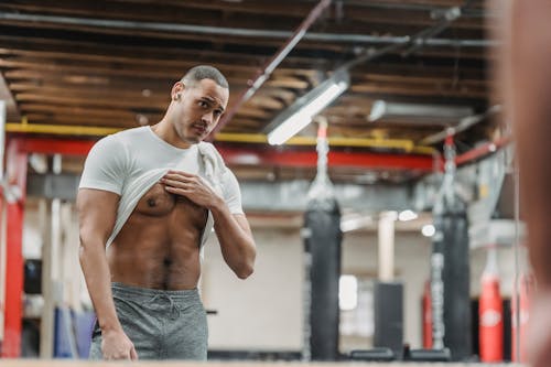 Fit ethnic sportsman demonstrating abs muscles in gym