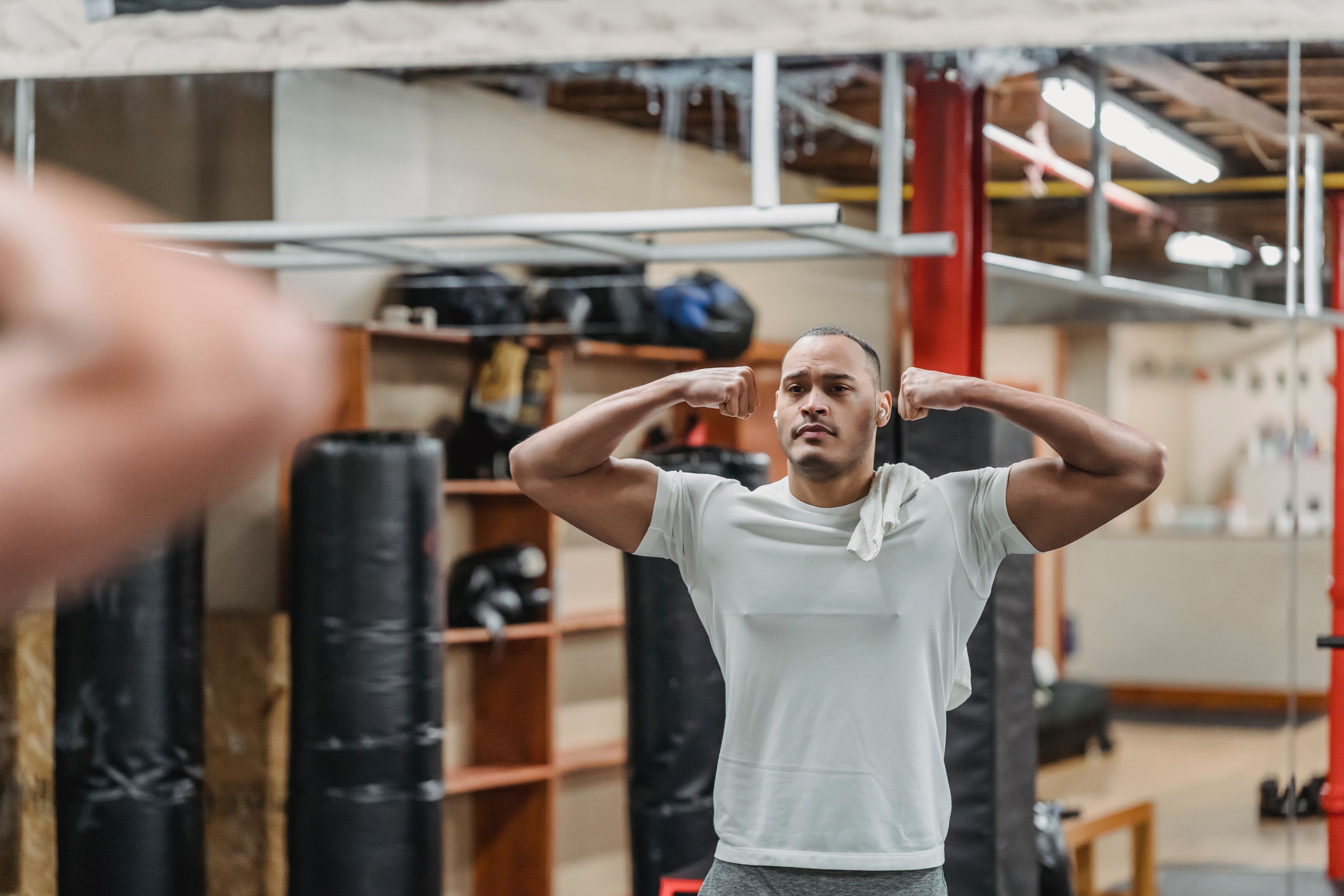 Muscular ethnic sportsman in white t shirt standing in double biceps pose and looking in mirror in modern quipped gym