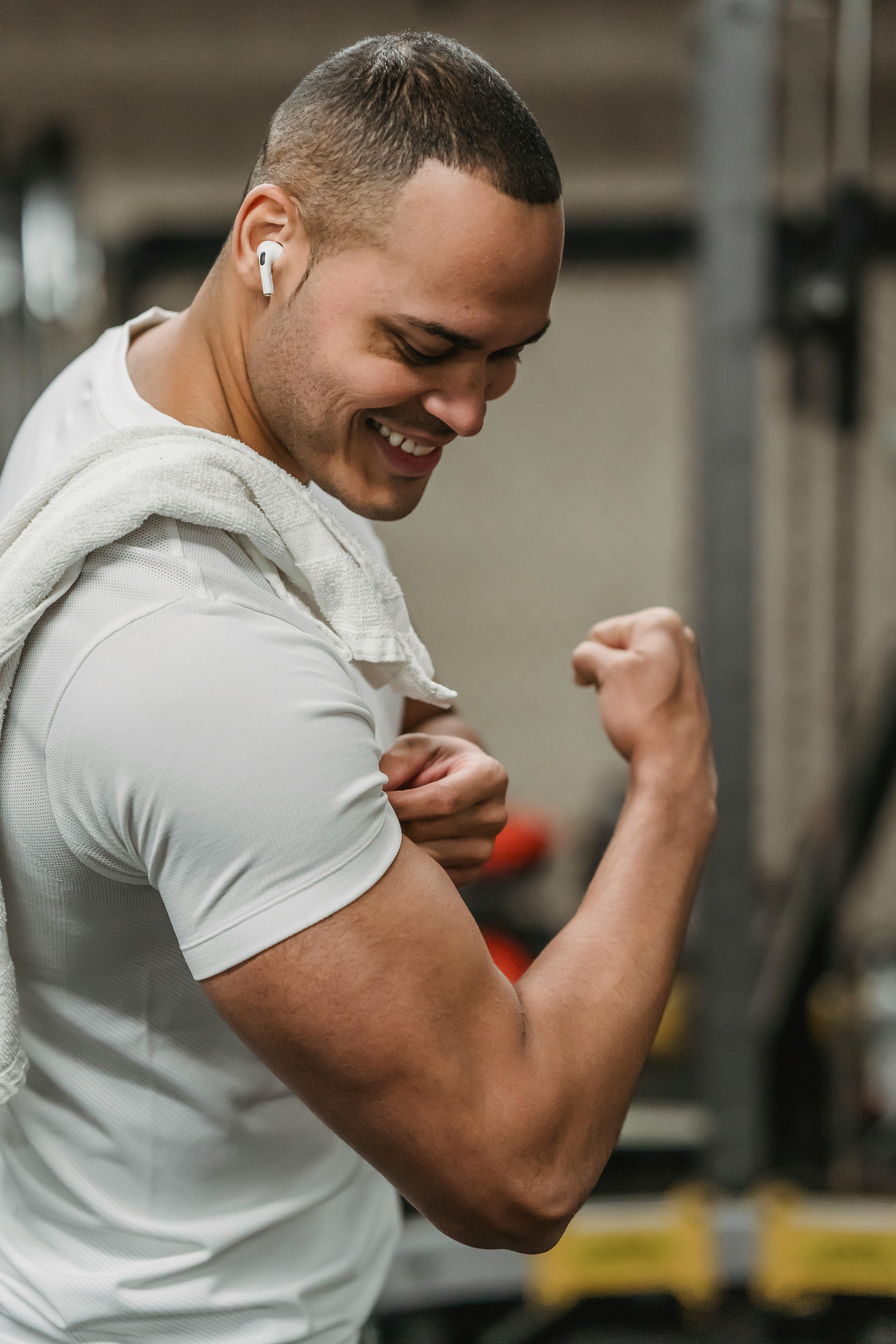 smiling muscular sportsman demonstrating biceps in gym