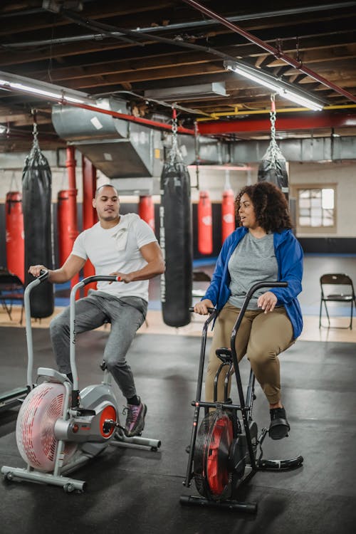 Diverse trainee and coach exercising on bicycles in gym