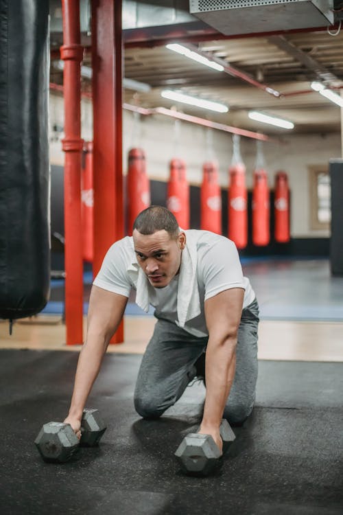 Strong ethnic sportsman exercising with dumbbells on gym floor