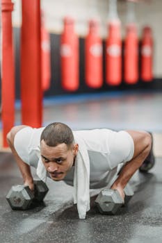 Concentrated muscular sportsman performing push ups on dumbbells in modern gym and looking away