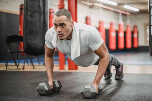 Free Muscular ethnic sportsman performing push ups with dumbbells in gym Stock Photo
