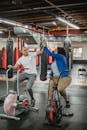 Full body plump black female trainee and sporty professional male fitness instructor clapping each others hands while riding stationary bicycles in modern gym