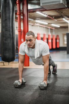Focused man engaged in intense workout with dumbbells in a gym setting with blurred background.