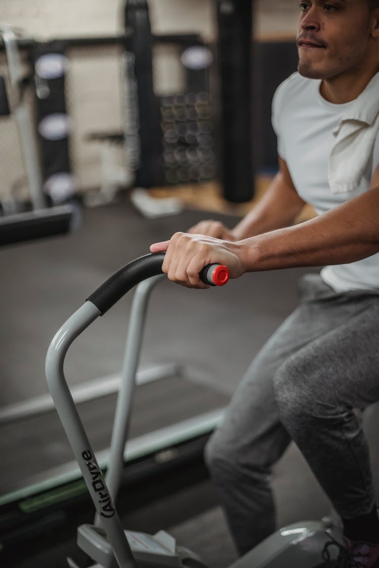 Crop Dedicated Ethnic Sportsman Exercising On Stationary Bike In Gym