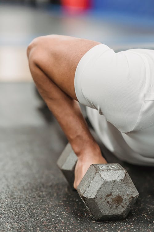 Free Crop anonymous muscular sportsman in white t shirt performing push ups with dumbbells in gym Stock Photo