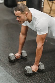 High angle of strong and concentrated ethnic male athlete doing tough exercise with dumbbells in gym