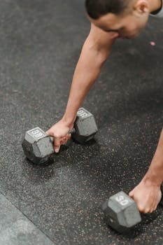 Focused male athlete lifting heavy dumbbells, highlighting strength and fitness in a gym setting.