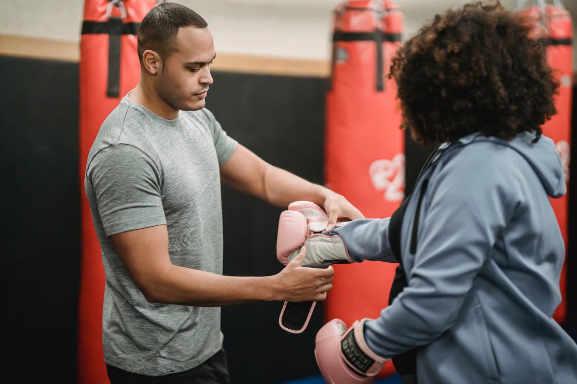 Free Side view of serious ethnic male coach helping plus size female putting on boxing gloves before training Stock Photo