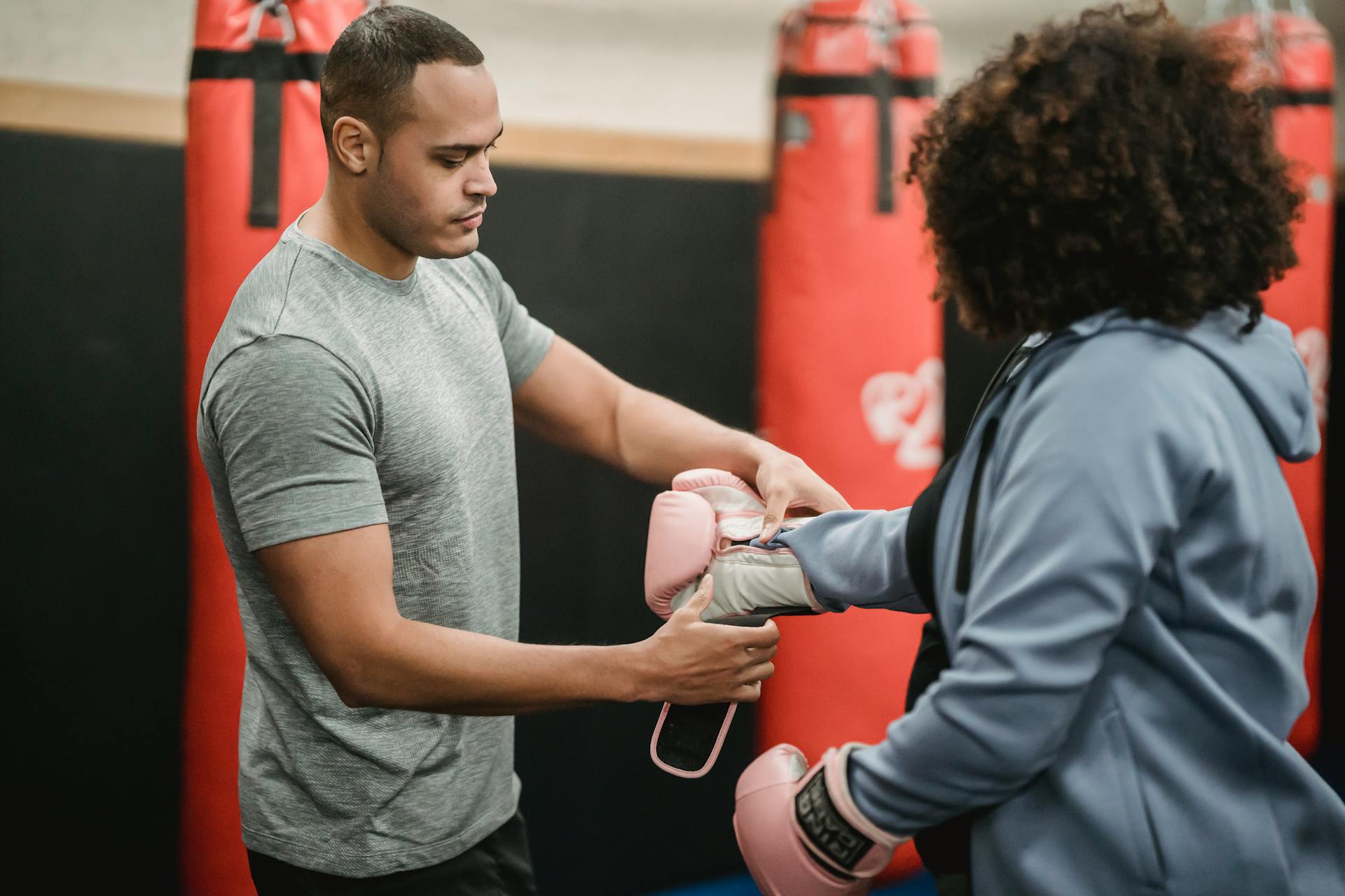 Side view of serious ethnic male coach helping plus size female putting on boxing gloves before training