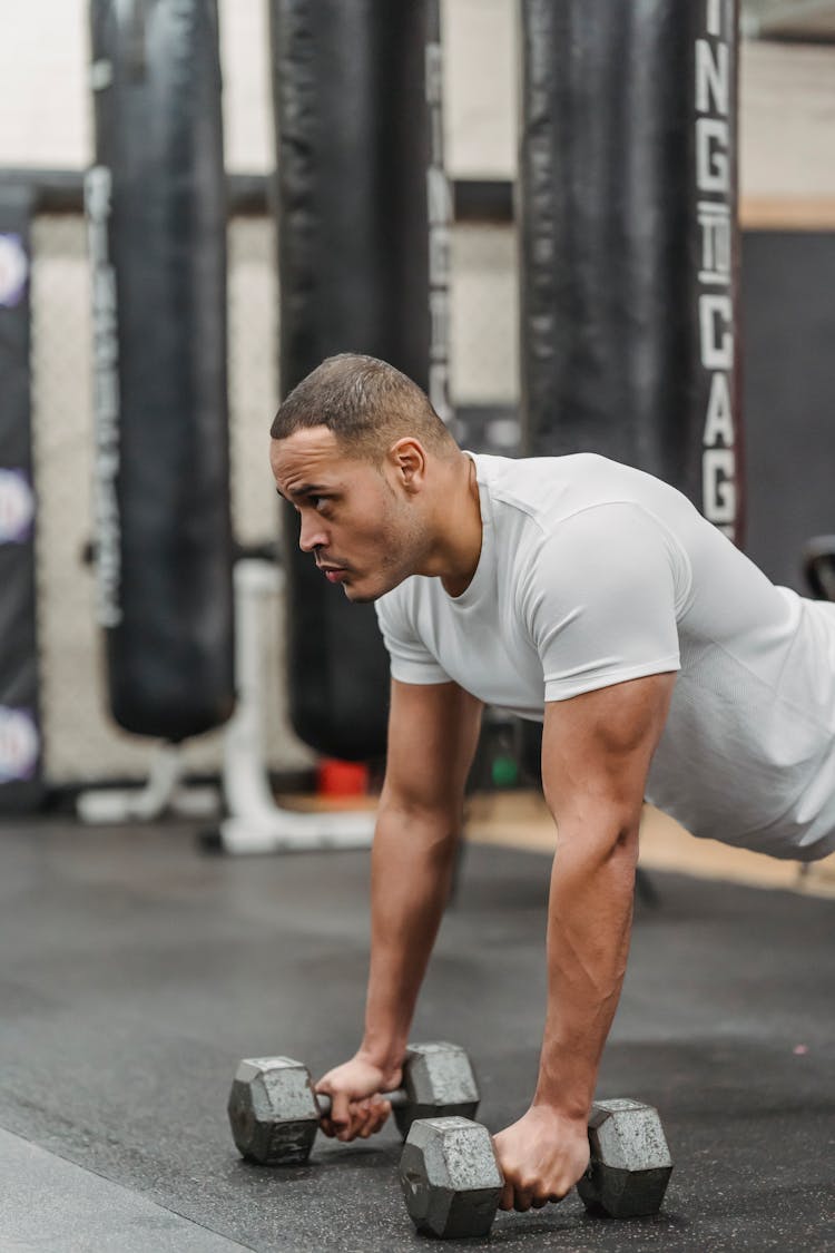 Muscular Ethnic Man Doing Plank With Dumbbells In Gym