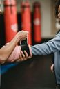 Side view of crop personal trainer preparing African American female for boxing training in gym with punching bags