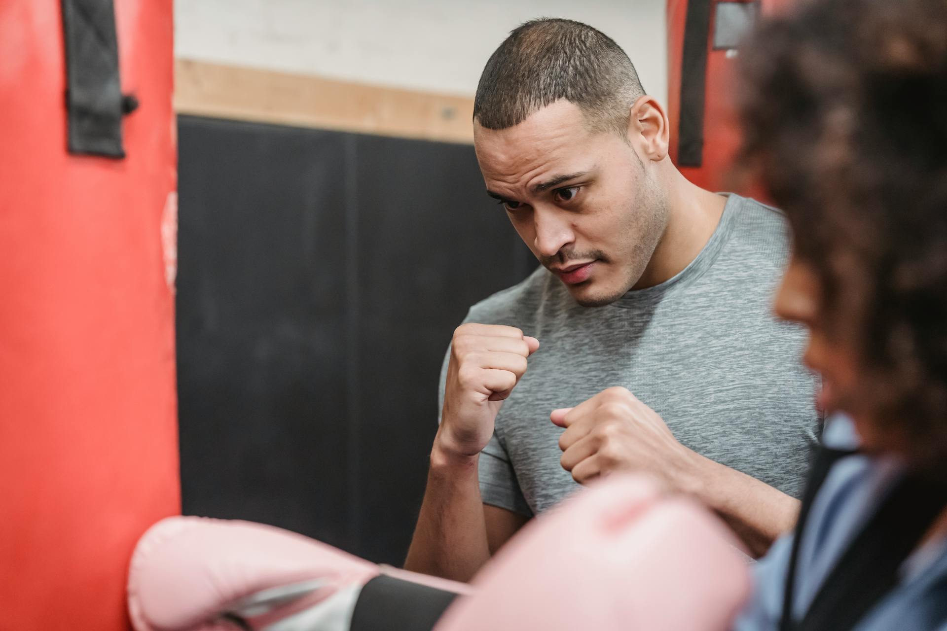 Entraîneur personnel ethnique concentré avec des poings s'entraînant avec une femme de culture frappant un sac de boxe pendant l'entraînement de boxe