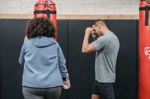 Free Sportive ethnic male trainer demonstrating position to female standing near punching bag during boxing workout Stock Photo