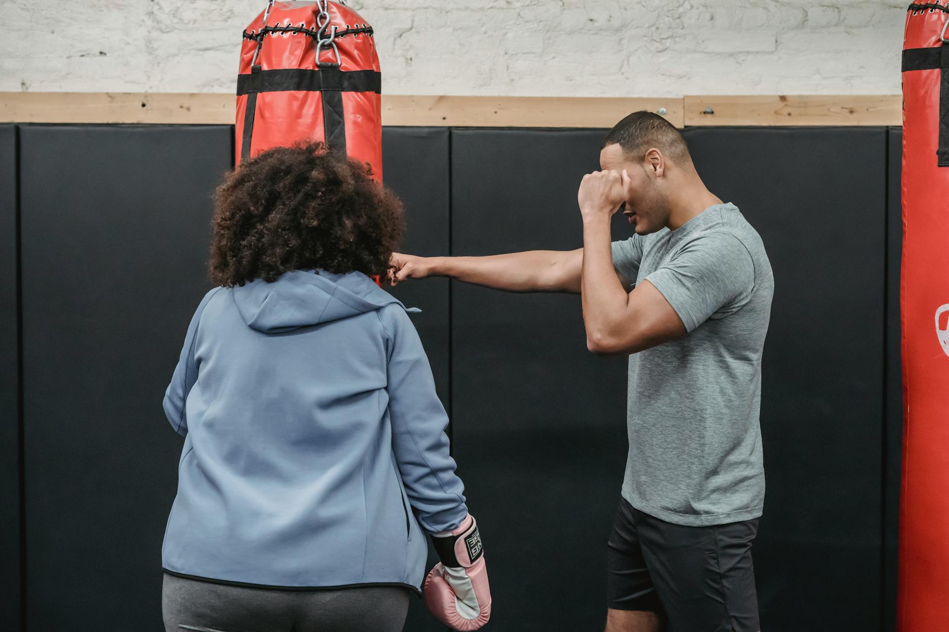 Ethnic trainer showing exercise to female in boxing club