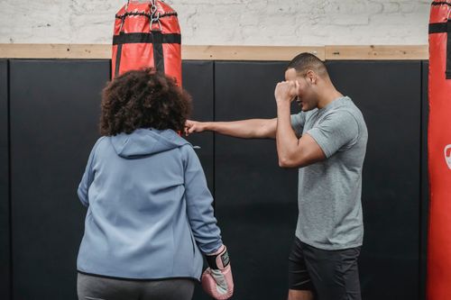 Free Focused ethnic male coach showing technique of hitting punching bag to overweight woman in boxing gloves Stock Photo