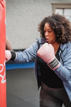 A determined woman practicing boxing with gloves in an indoor gym setting, showcasing strength and focus.