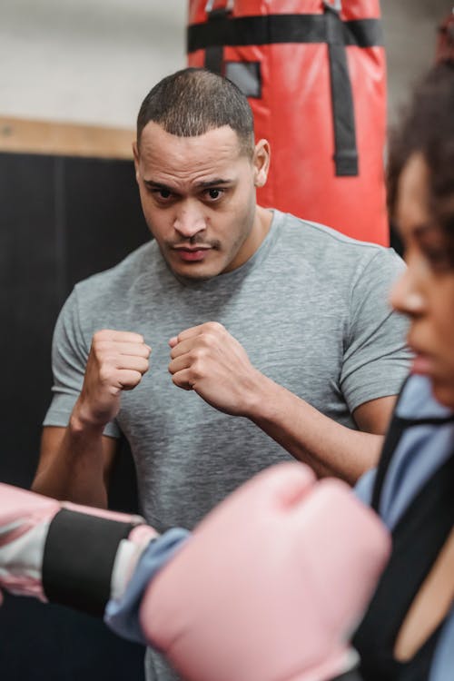 Concentrated ethnic male coach training with crop African American female in boxing gloves in gym