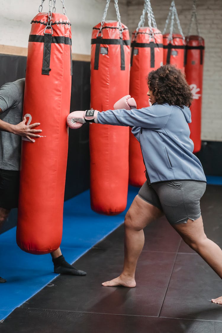 Strong Woman Punching Boxing Bag During Training With Trainer