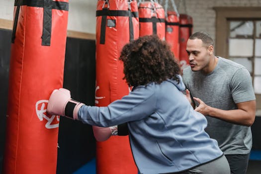 A woman practices boxing with a coach guiding her during a workout session in the gym.