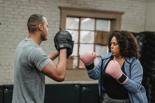 A focused female boxer trains with a male coach in a gym, showcasing strength and determination.