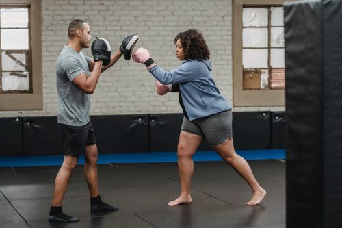 Free Side view of concentrated overweight African American female in boxing gloves hitting personal trainer during workout Stock Photo