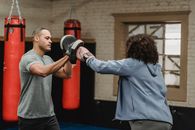 Ethnic trainer working out with unrecognizable boxer in gym