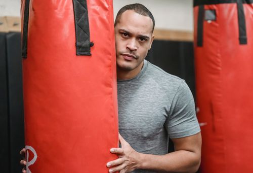 Free Adult serious ethnic male athlete with muscles in t shirt looking at camera between punching bags in gymnasium Stock Photo