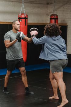 Ethnic instructor fighting with unrecognizable boxer in gym
