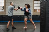 Ethnic male instructor with focus mitts combating with overweight African American female athlete while practicing boxing in gymnasium