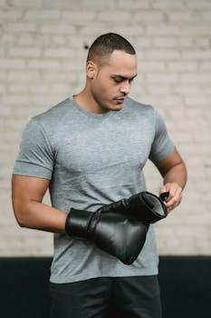 Muscular young man wearing boxing gloves preparing for a workout session indoors.