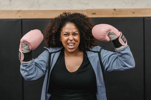 Excited young black sportswoman showing biceps after boxing training